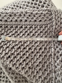 a person measuring the size of a grey knitted blanket