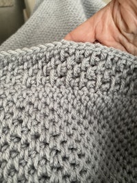 a person holding a grey crocheted blanket