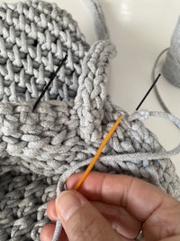 a person knitting a grey sweater with a needle