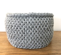 a grey knitted basket on top of a wooden table