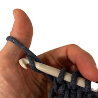 a person holding a crochet hook in a blue yarn